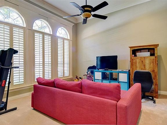 The living room with windows looking out to the front yard.  Plantation shutters, ceiling fan, carpet and extra wide crown molding.  This room is located to the right of the entry way and could also be used as a study.