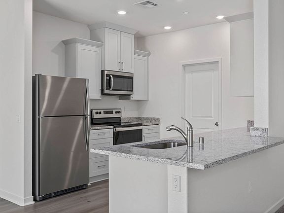 The kitchen has stainless steel appliances and plank flooring.