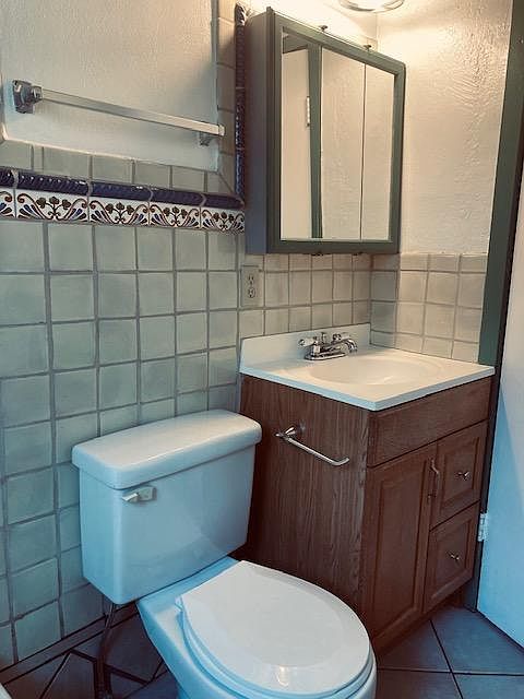 full bathroom with sink and mirrors, toilet, tub, Mexican tiles, and plain tile flooring