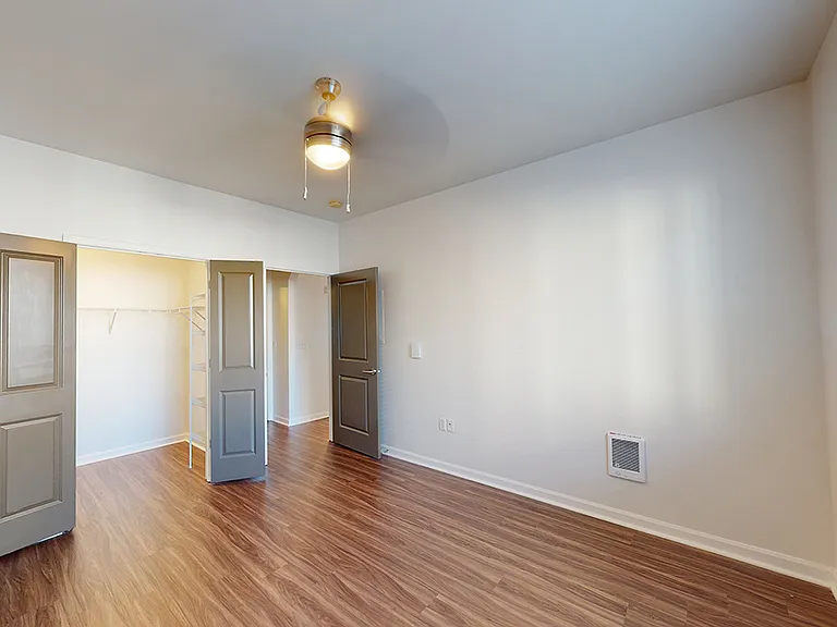 Spacious apartment bedroom with large closet and wood-style flooring.