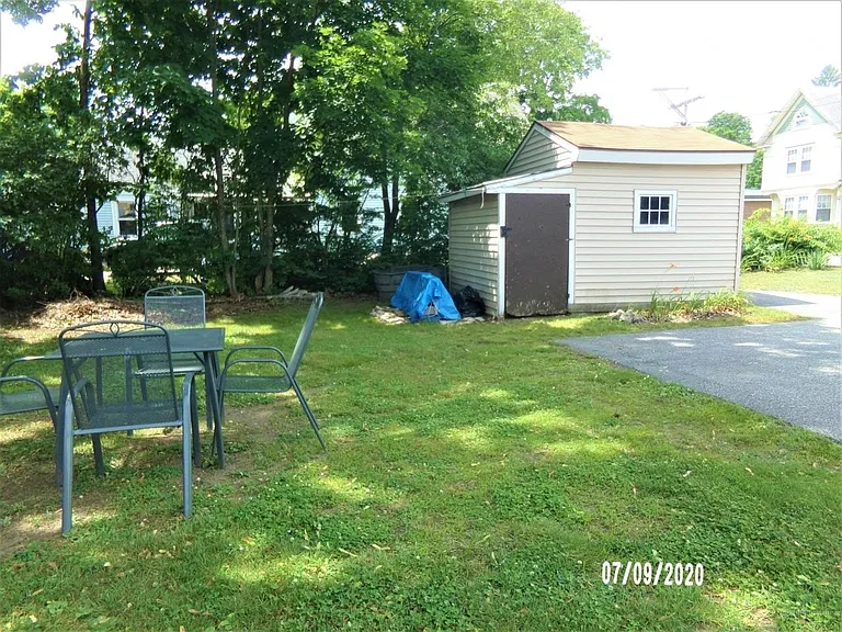Backyard with tarred parking area. Small shed for rakes, shovels, and mower.
