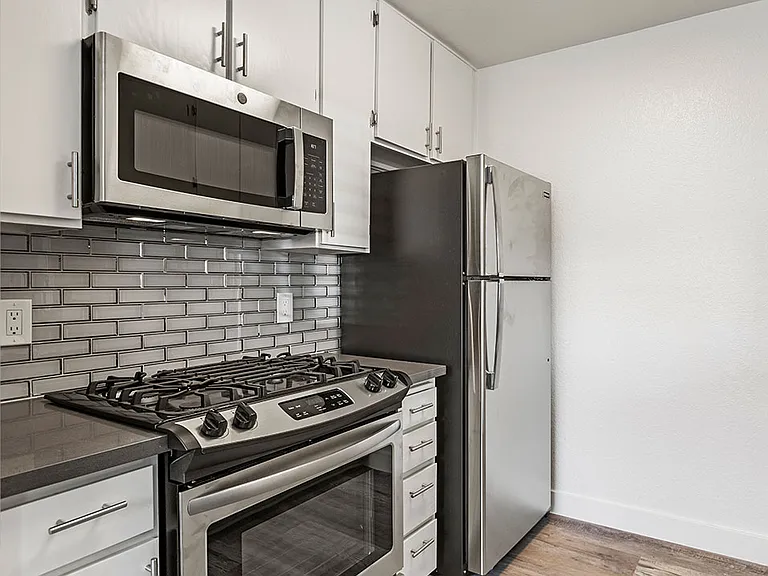 White tiled kitchen with stainless steel fridge, oven, and microwave.