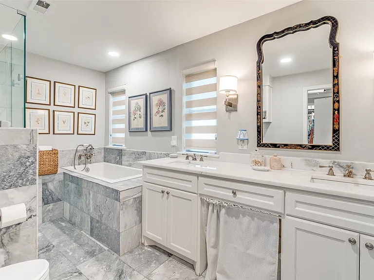 Bathroom featuring dual vanities with white cabinetry, white countertops, and wall-mounted sconces