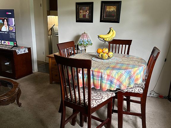 To one side, the dining area sits comfortably within the same open footprint, defined subtly by a statement light fixture above a large dining table that seats four to six guests.