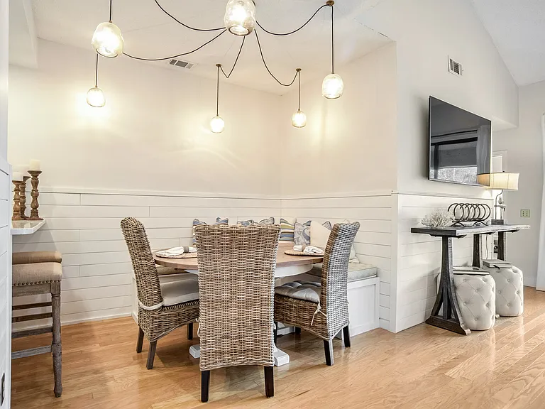 Gather around in this inviting dining space with custom lighting, a built-in bench, and woven chairs that add a touch of coastal elegance. The perfect spot for family meals or entertaining guests.