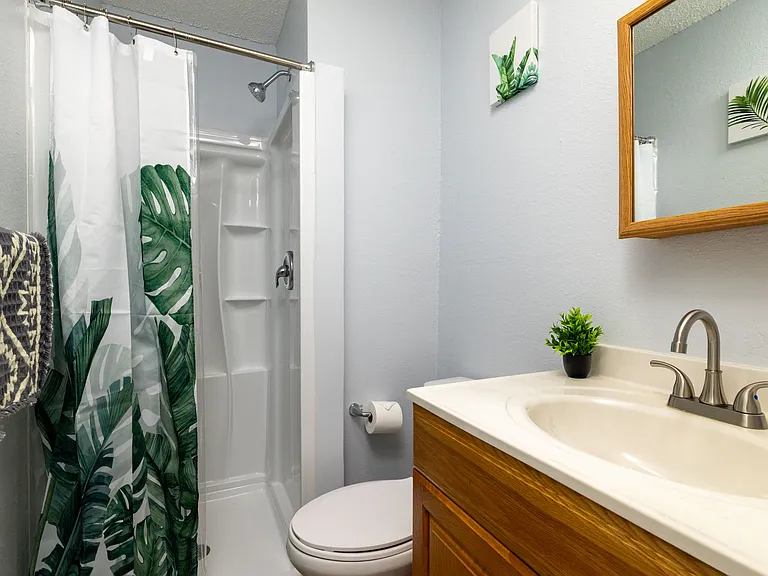 Bright second bathroom featuring a walk-in shower with a tropical leaf curtain.