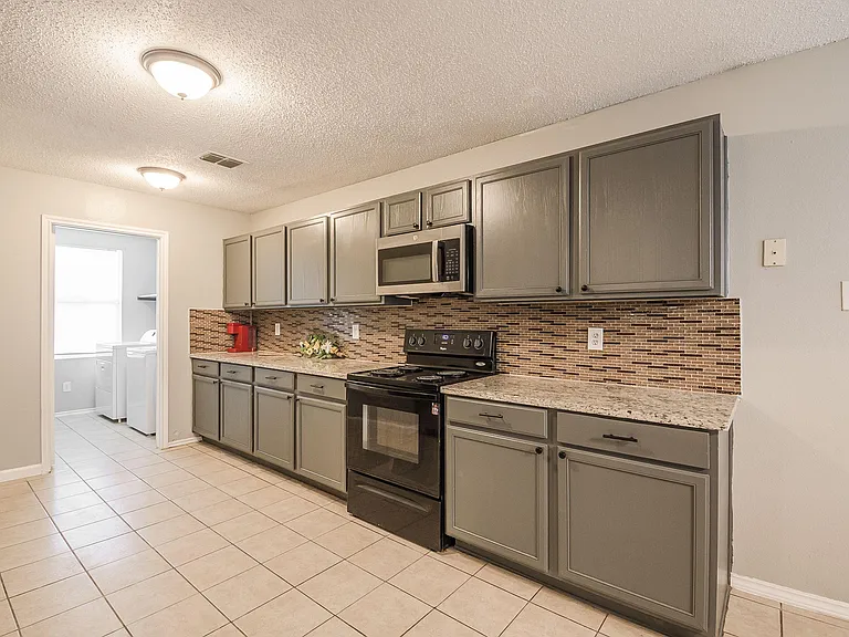 Functional galley kitchen with ample cabinetry, tile flooring, mosaic backsplash, and a full appliance package.