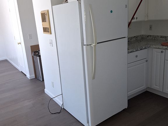 Side view of the brand new refrigerator and looking partially into the living room with the storage closet of the living room in the background