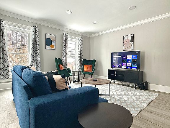 This cozy living room features a deep sofa, two chic accent chairs, and plenty of natural light, creating a bright, airy space perfect for relaxing or enjoying your favorite shows.