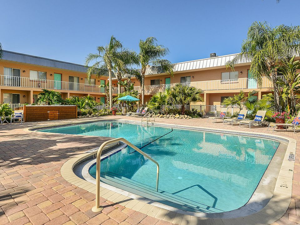 Inviting pool area surrounded by lush palm trees and vibrant outdoor seating at a charming apartment complex.
