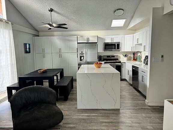 Spacious open concept living area with conversation area, kitchen and dining with ample cabinetry, ceiling fan, and center island with storage.