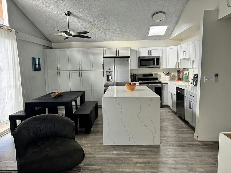 Spacious open concept living area with conversation area, kitchen and dining with ample cabinetry, ceiling fan, and center island with storage.