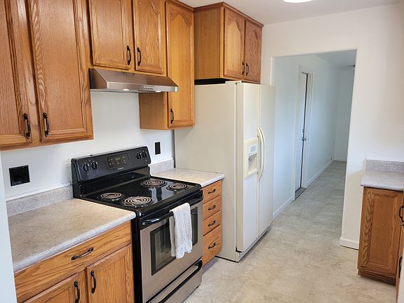 Kitchen, range, and refrigerator. Past that is utility room with laundry hookups, and door to garage.