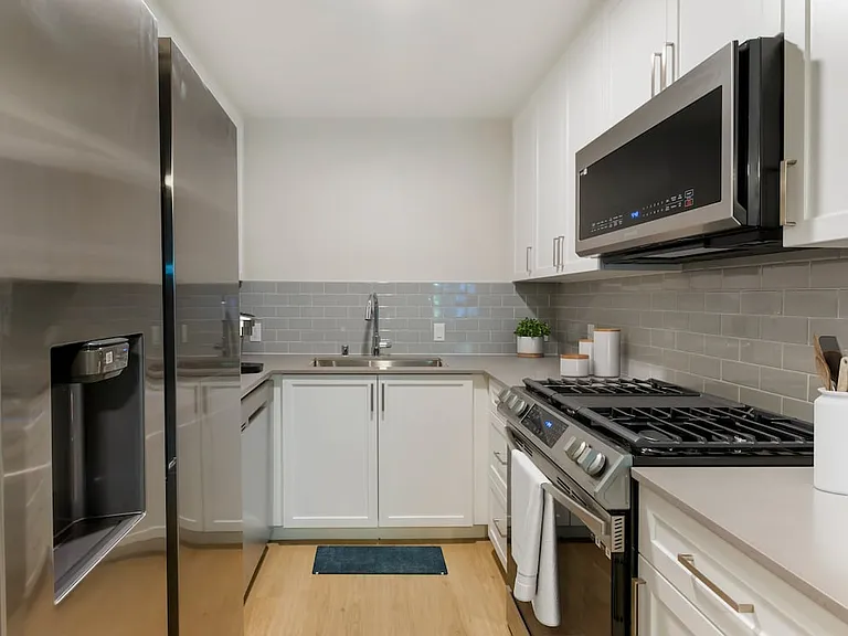 Kitchen with white cabinetry, grey quartz countertops, stainless steel appliances, grey tile backsplash, and hard surface flooring (Select Home)