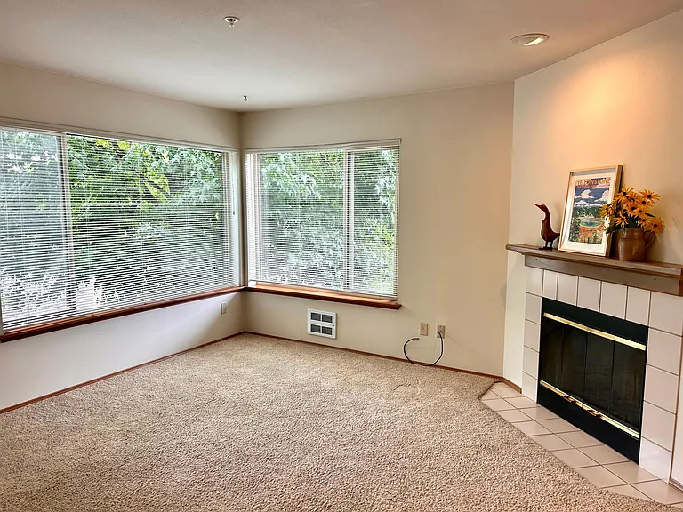 Living area with large windows and fireplace with wooden mantel.