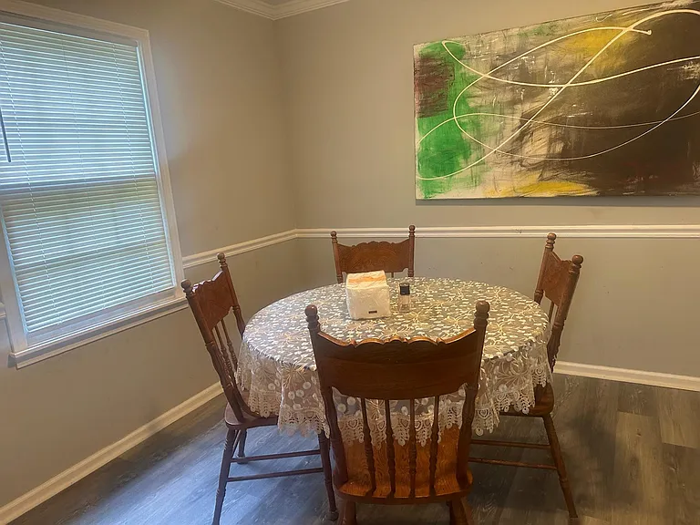 Dedicated dining area with a round table, seating for four, and a large window with blinds for natural light.