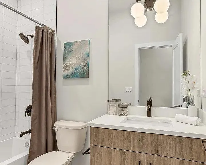 Bathroom (Angle 1): Fresh and modern full bath with wood-tone vanity, white quartz countertop, and globe pendant lighting