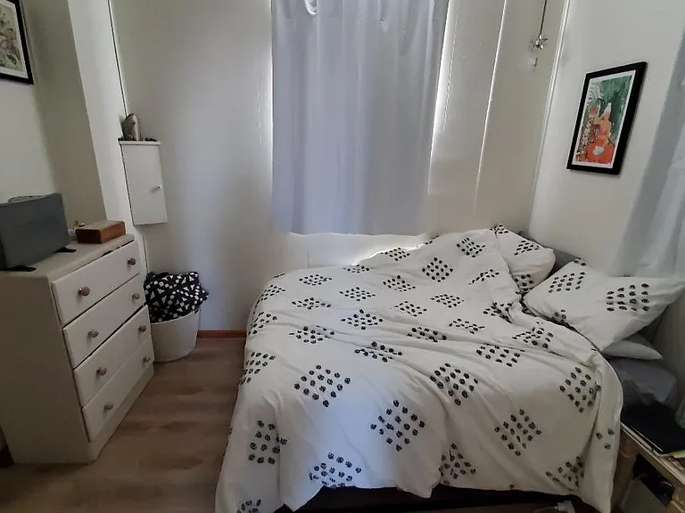 Bedroom fits a queen size bed. This is different tenant, with bed on a different wall than previous photo. Living room behind photographer.