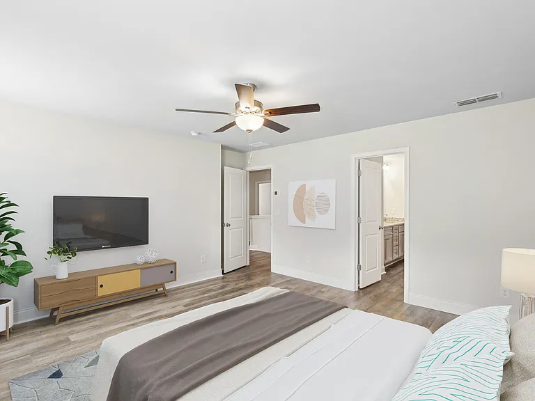 Another perspective view of the serene primary suite, showcasing a modern ceiling fan, sleek entertainment, and sunlit window views.