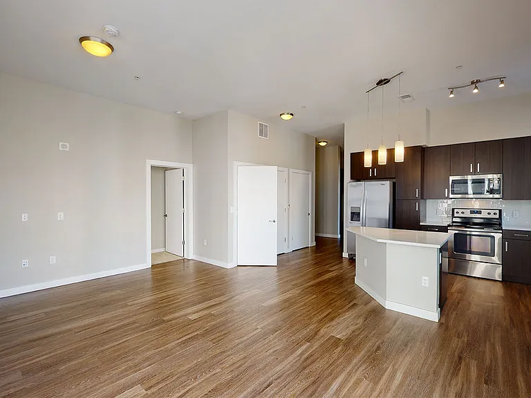 Apartment kitchen with stainless steel appliances, dining and living room with wood-style flooring.
