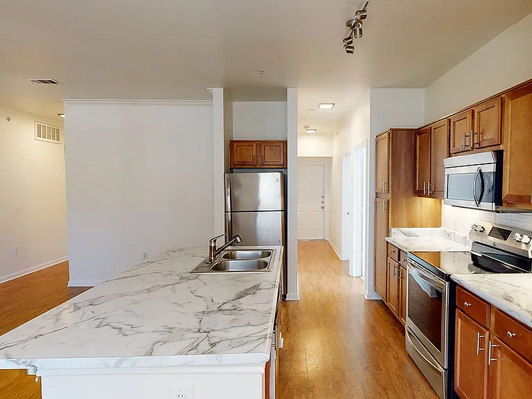 Apartment kitchen with stainless steel appliances, wood-style flooring, and marble-style countertops (shown here). Quartz-style countertops are available in select homes.