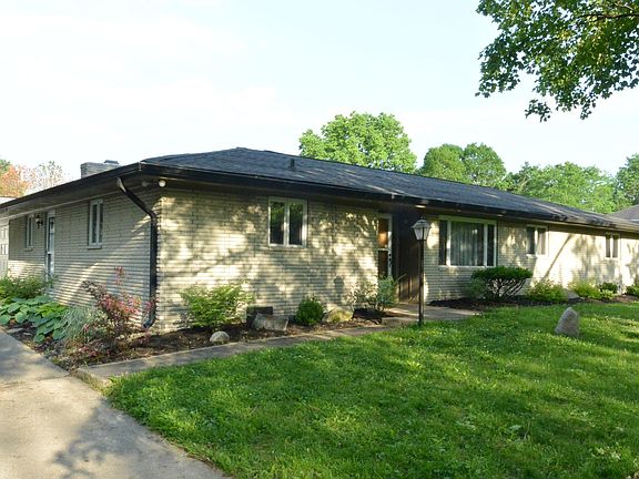 Front of house from driveway. Lots of bushes and hostas in flower beds.