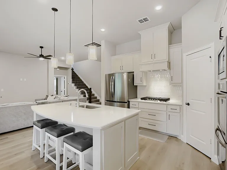 Contemporary kitchen featuring a large island with seating, white shaker cabinetry, stainless steel appliances, and wood-finish flooring