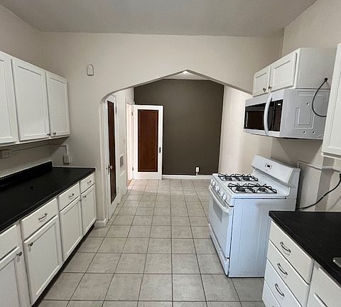 Kitchen view from the back entrance. New cabinets, microwave, countertops. Arch and accent wall in dining area