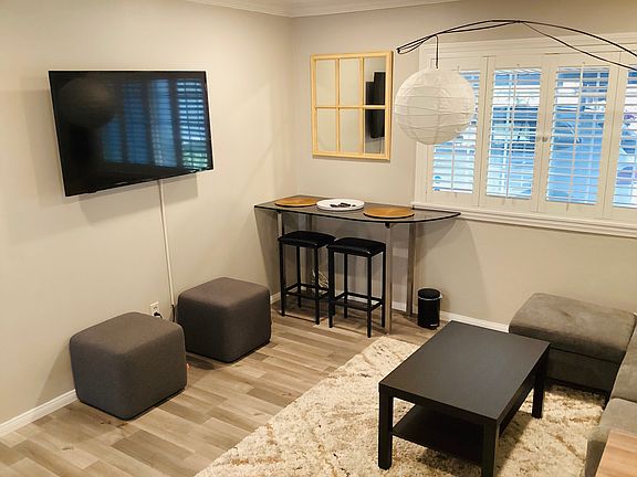 Sunny living room with bar table and stools for dinning, sturdy ottomans for extra seating and smart t.v. for movie night.