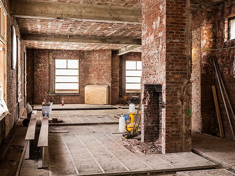 Before: Well-lit room surrounded by windows and adorned in exposed brick during renovation