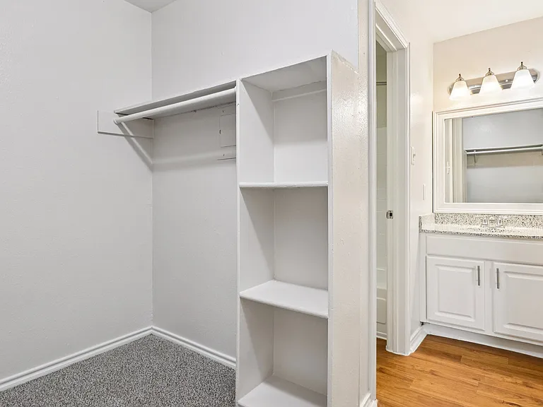 Elegant walk-in closet with built-in shelving adjacent to a bright bathroom featuring a modern vanity and sleek lighting. Elegant walk-in closet with built-in shelving adjacent to a bright bathroom featuring a modern vanity and sleek lighting.