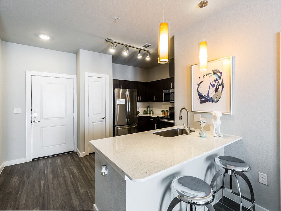 Kitchen island with white quartz countertops, modern lighting fixtures looking into kitchen