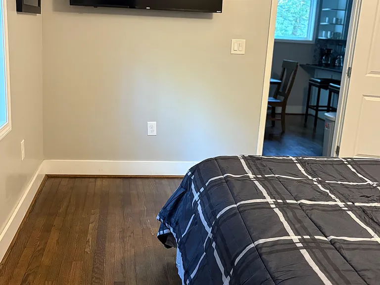 Private bedroom with hardwood floors, wall-mounted TV, and quick access to the shared kitchen and dining area.