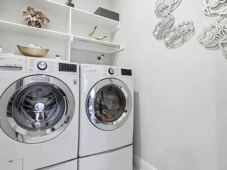 Dedicated laundry space with white built-in shelving, white walls, and a white baseboard trim.