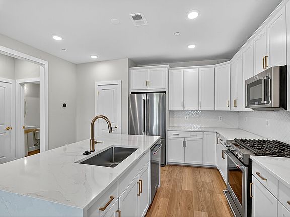 A modern, well-lit kitchen with white cabinets, stainless steel appliances, and a marble countertop