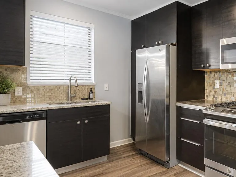 Updated kitchen with dark cabinetry, granite counters, mosaic tile backsplash, and stainless steel appliances.