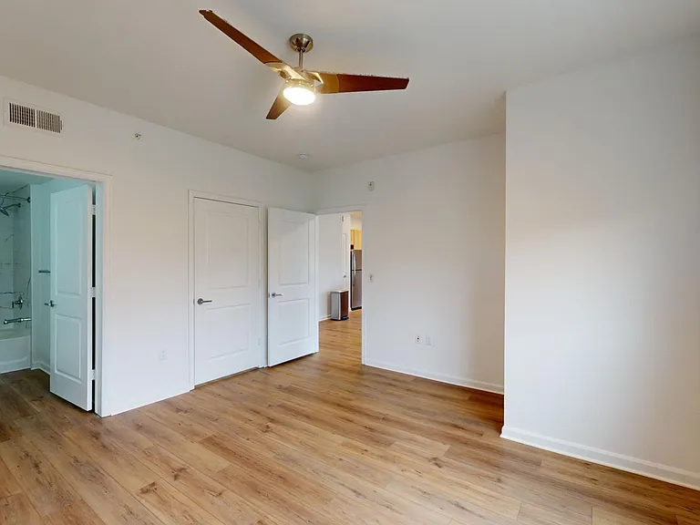 Spacious apartment bedroom with attached bathroom and wood style floor.
