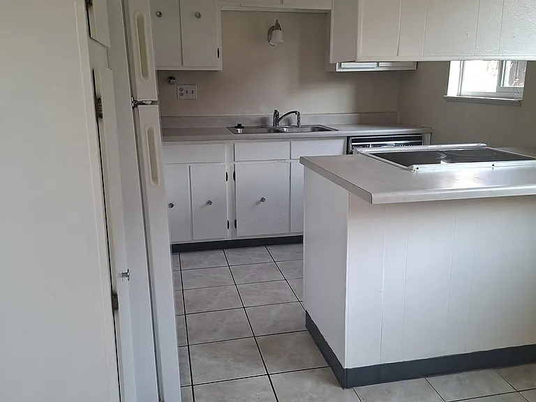 Looking directly to the Kitchen from Dining room, again with tile floor throughout. Shows dishwasher (to the right of faucet), refrigerator and glass top stove. Efficiency washer and dryer unit located behind the refrigerator on left side.