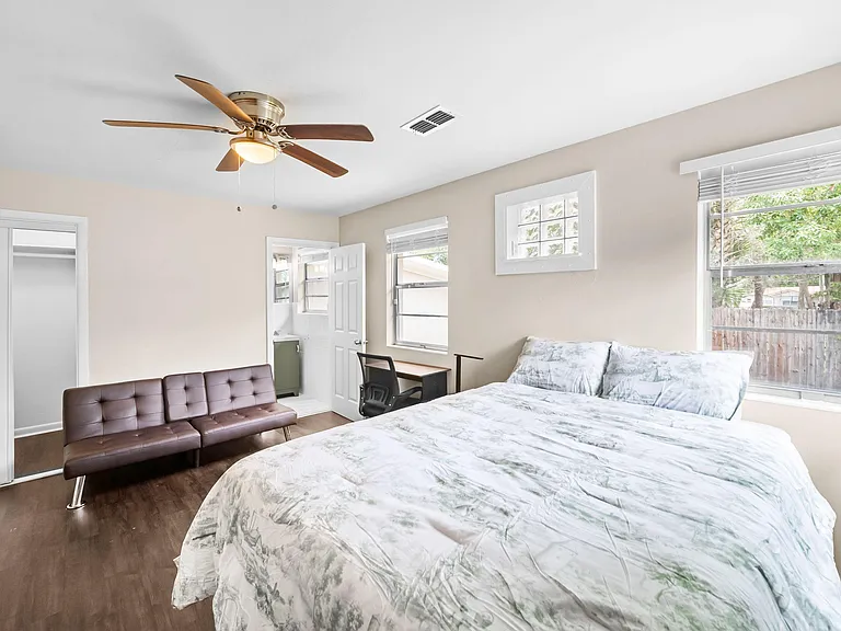 Furnished bedroom with a full bed, futon, and desk, plus a closet and windows for natural light and ventilation.