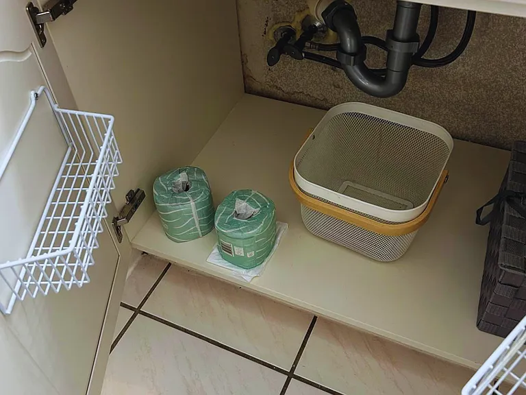 Bathroom cabinet stocked with toilet paper and trash bags.