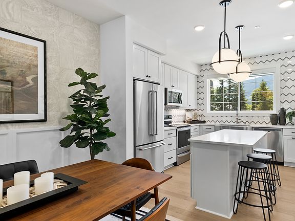A modern, well-lit kitchen with white cabinets, stainless steel appliances, and a wooden dining tabl