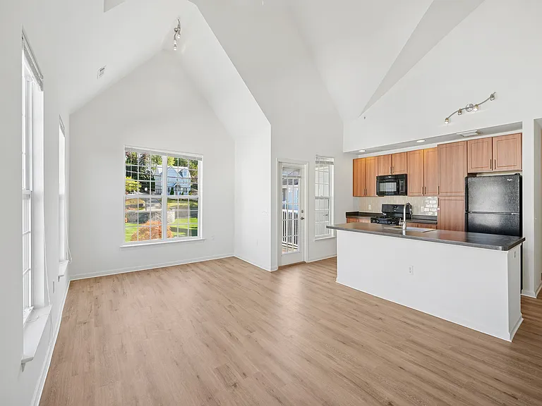Bright and airy open-concept living space with vaulted ceilings, modern kitchen with wooden cabinetry, and sleek flooring, featuring large windows that offer scenic views.