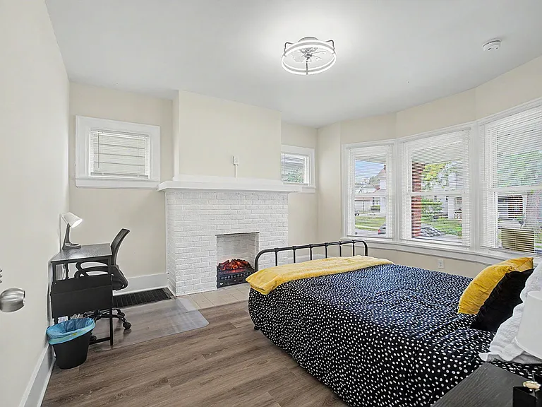 Spacious bedroom with bay windows, wood-look flooring, and a decorative fireplace, plus room for a desk or seating area.