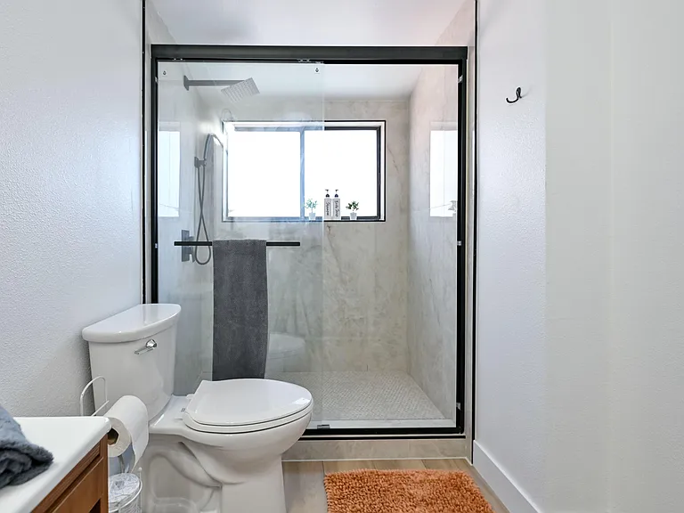 Updated bathroom with a glass-enclosed walk-in shower, rainfall showerhead, and window for fresh air and light.