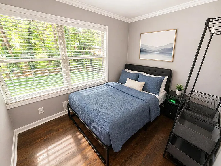 Well-proportioned bedroom with a large window, hardwood floors, and space for a bed plus shelving or a nightstand.