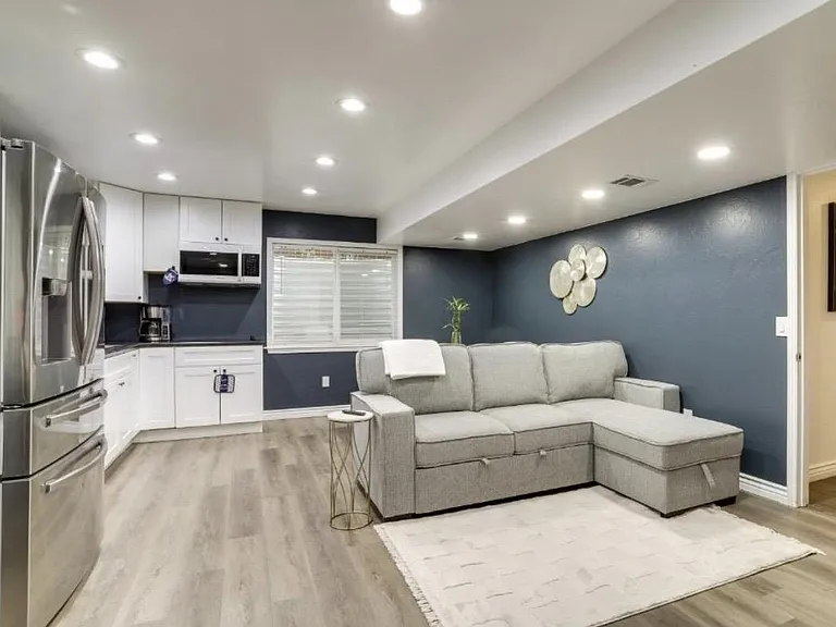 Open-concept living area with recessed lighting, large window, and an adjacent kitchen featuring white cabinetry and stainles