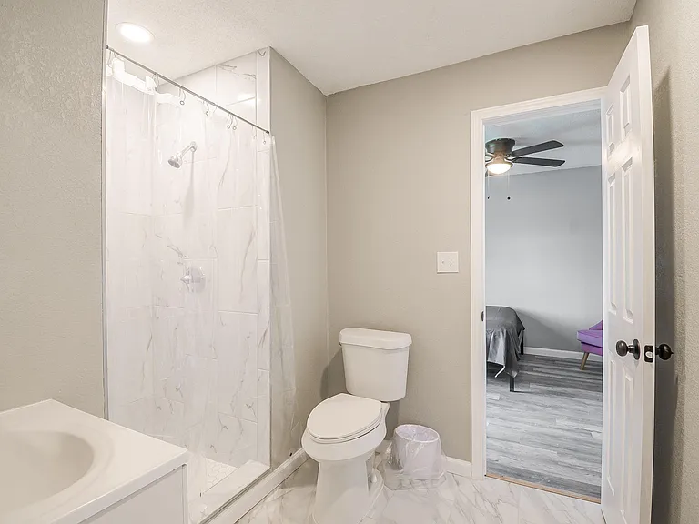 Clean full bath with tiled shower/tub surround, vanity sink, and easy-care flooring with nearby bedroom access.