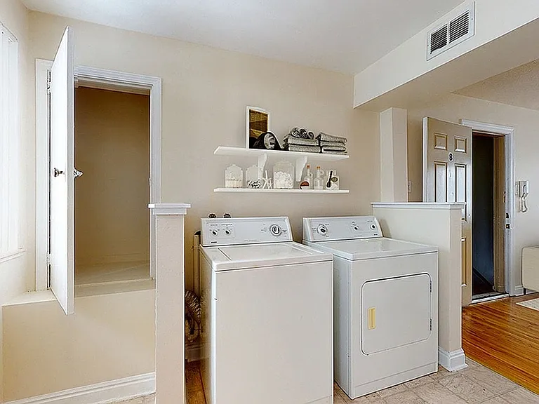 Bright laundry room with modern washer and dryer, accented by sleek shelving for stylish storage. Adjacent cozy living space with contemporary decor.