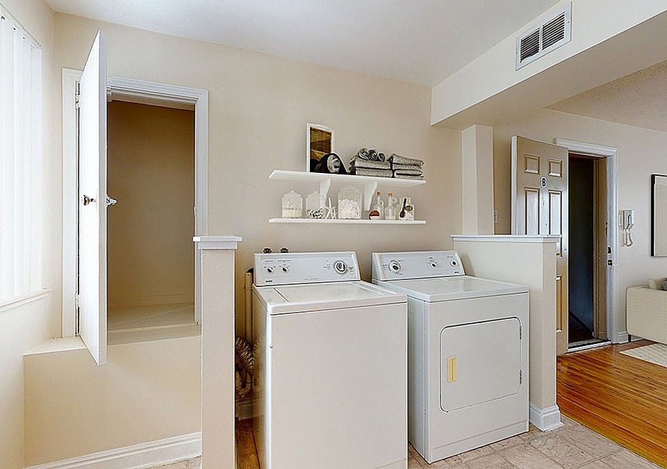 Bright laundry room with modern washer and dryer, accented by sleek shelving for stylish storage. Adjacent cozy living space with contemporary decor.