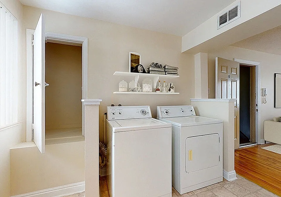 Bright laundry room with modern washer and dryer, accented by sleek shelving for stylish storage. Adjacent cozy living space with contemporary decor.